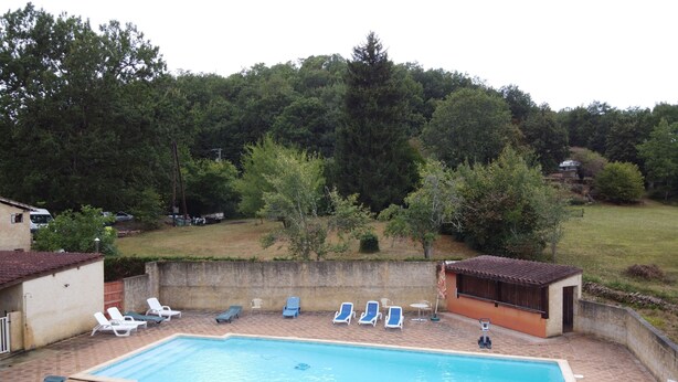 Ein rechteckiger Swimmingpool mit einer gefliesten Liegefläche, umgeben von Liegestühlen und einem kleinen überdachten Bereich.
