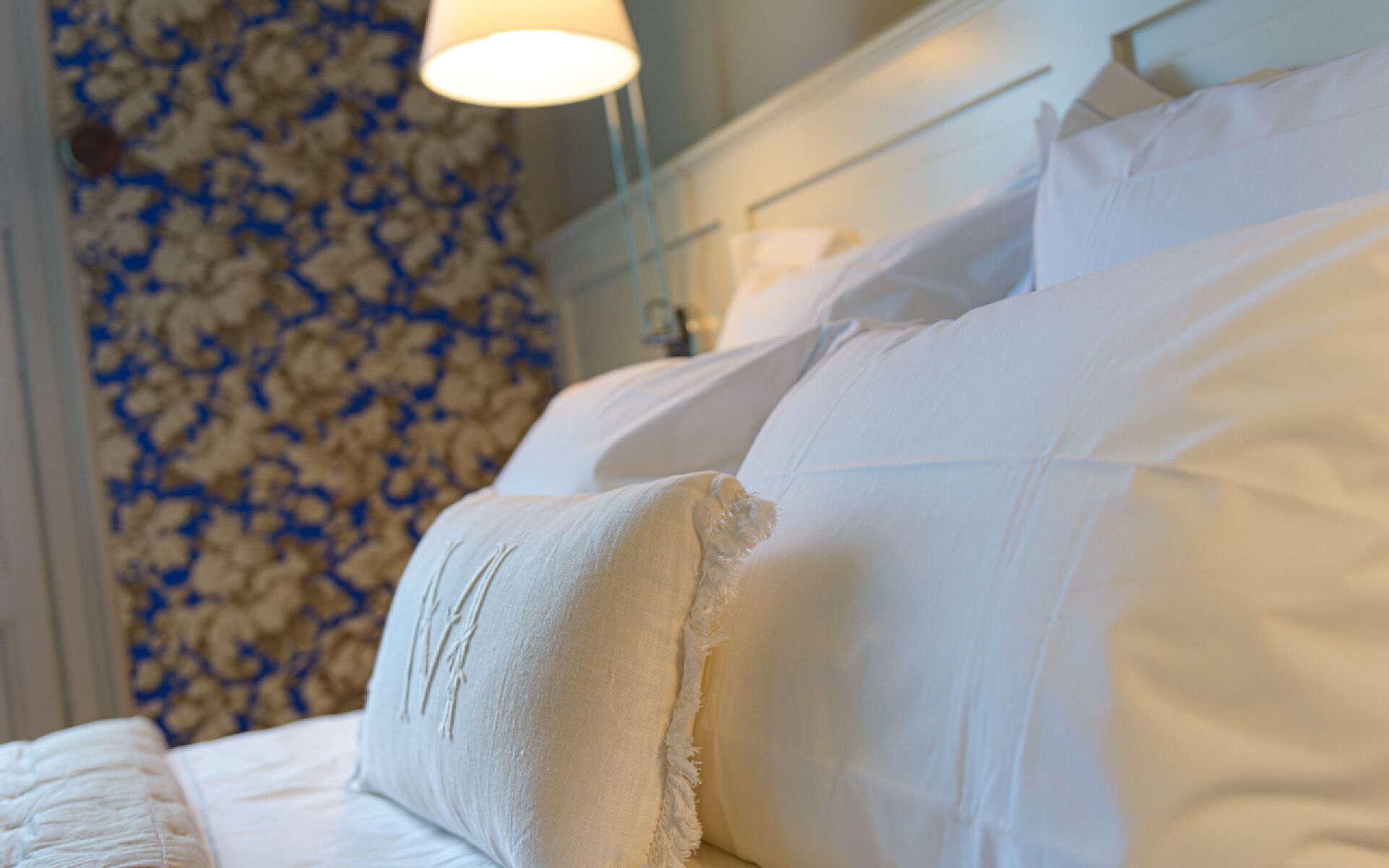 Een net opgemaakt bed met witte lakens en een gestructureerde muur erachter.