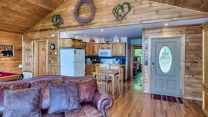 Un accogliente interno di una baita con soffitto in legno, un divano in pelle, angolo cottura e tavolo da pranzo.
