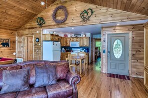 L’intérieur chaleureux d’un chalet avec un plafond en bois, un canapé en cuir, un coin cuisine et une table à manger.