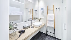 Un bagno moderno con uno specchio grande, un lavabo, un portasciugamani e un asciugacapelli sul ripiano.