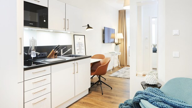 Una cucina moderna con mobili bianchi, un piano cottura nero e un'area pranzo con tavolo e sedie.