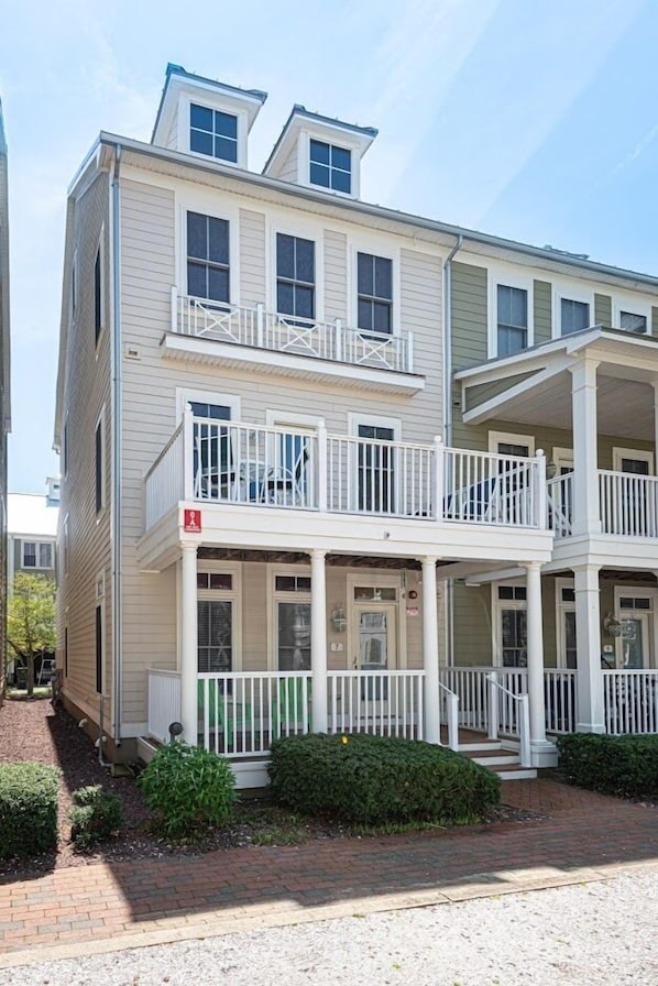 A two-story building with a balcony on the second floor, a front porch, and a small garden area.
