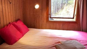 Ein Zimmer in einer Holzhütte mit einem Bett, einem Fenster und einer Wandleuchte.