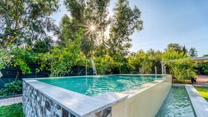 Una piscina rectangular con borde de piedra, rodeada de abundante vegetación y árboles.