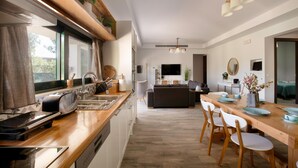 Cocina moderna con tostadora, pileta y encimera de madera. Hay un comedor con mesa y sillas, y una sala de estar con sofá y televisor.