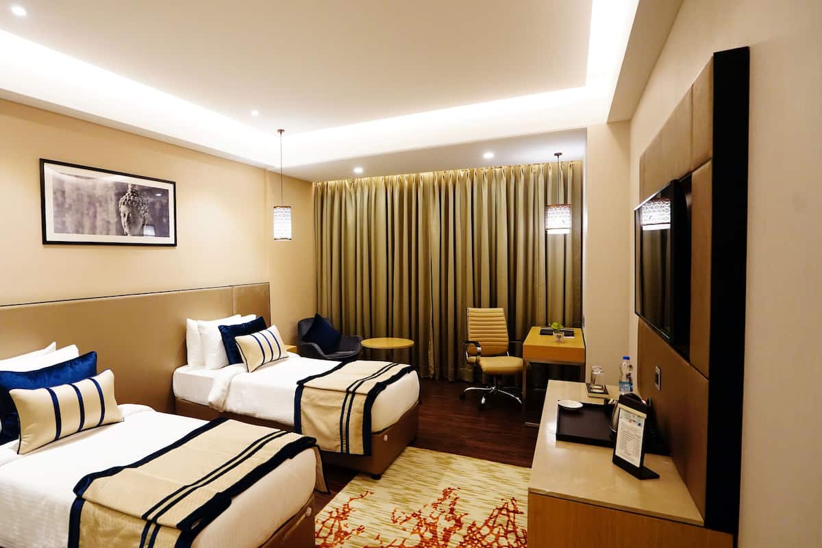 A hotel room with two beds, a desk, a chair, a TV, and a curtain.