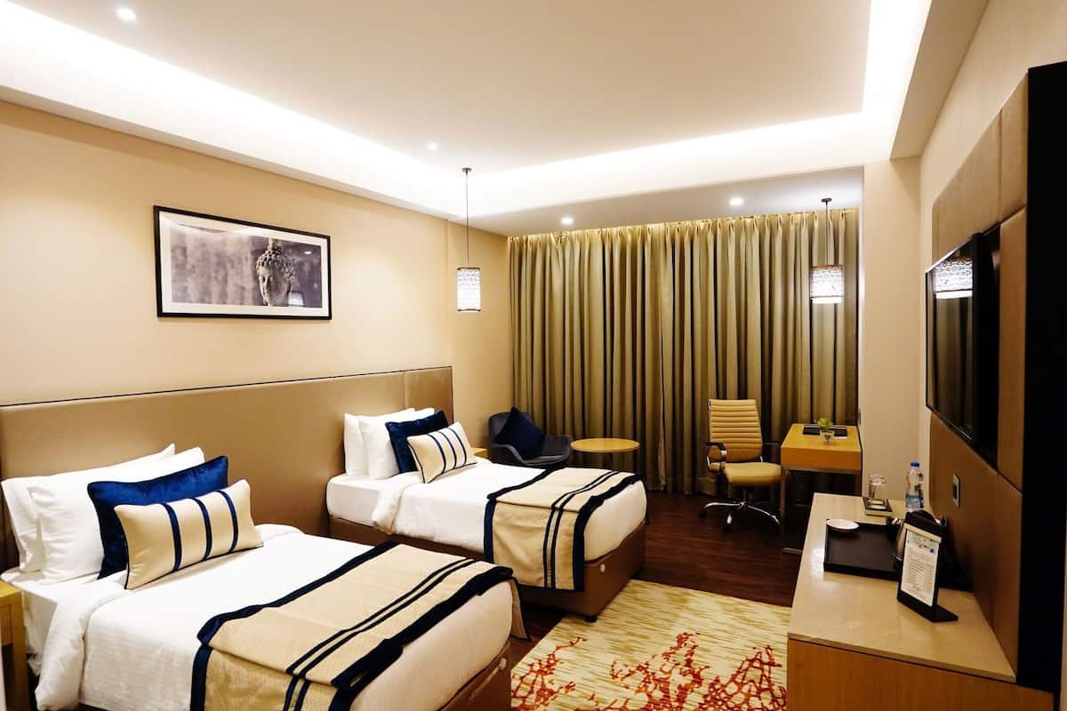 A hotel room with two beds, a desk, a chair, a television, and a curtain.