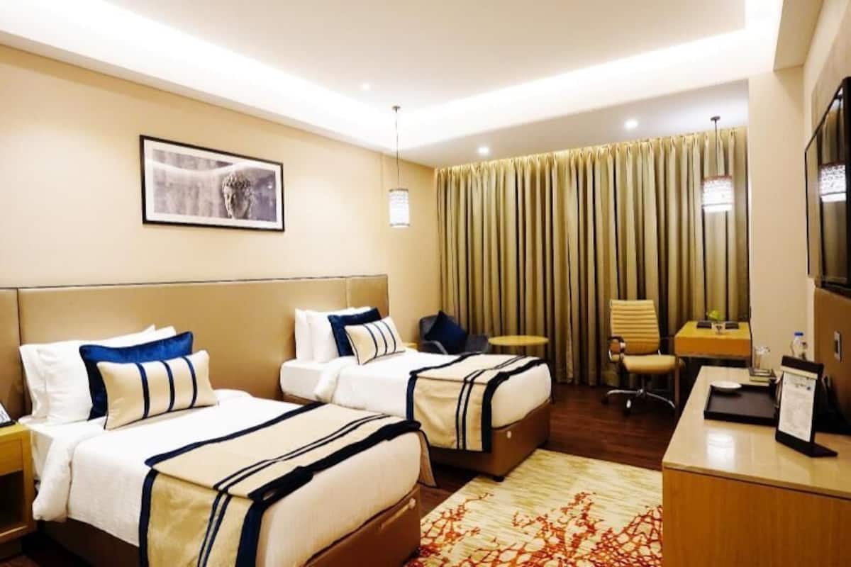 A hotel room with two beds, a desk, a chair, a TV, and a window with curtains.