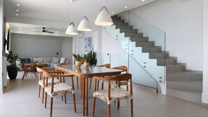A modern living room with a dining area, featuring a glass staircase and contemporary furniture. - Rozites Luxury Beachfront Villa, By Hellocrete (Agia Foteini)