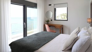 A hotel room with a bed, a desk, a chair, a potted plant, a mirror, and a view of the sea. - Rozites Luxury Beachfront Villa, By Hellocrete (Agia Foteini)