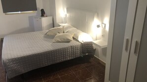 A neatly made bed with a patterned bedspread and pillows, a bedside table with a lamp, and a wardrobe. - TAMONANTE HOSTEL (Gran Tarajal)