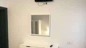 A room with a white desk, a chair, a flat-screen TV mounted on the wall, and a mirror above the desk. - TAMONANTE HOSTEL (Gran Tarajal)
