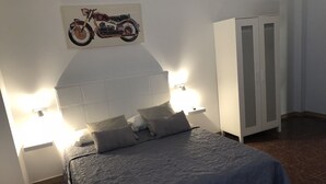 A bedroom with a bed, pillows, a headboard, a cabinet, and a motorcycle artwork on the wall. - TAMONANTE HOSTEL (Gran Tarajal)