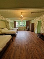 A room with three beds, a chandelier, a window with curtains, and a door.