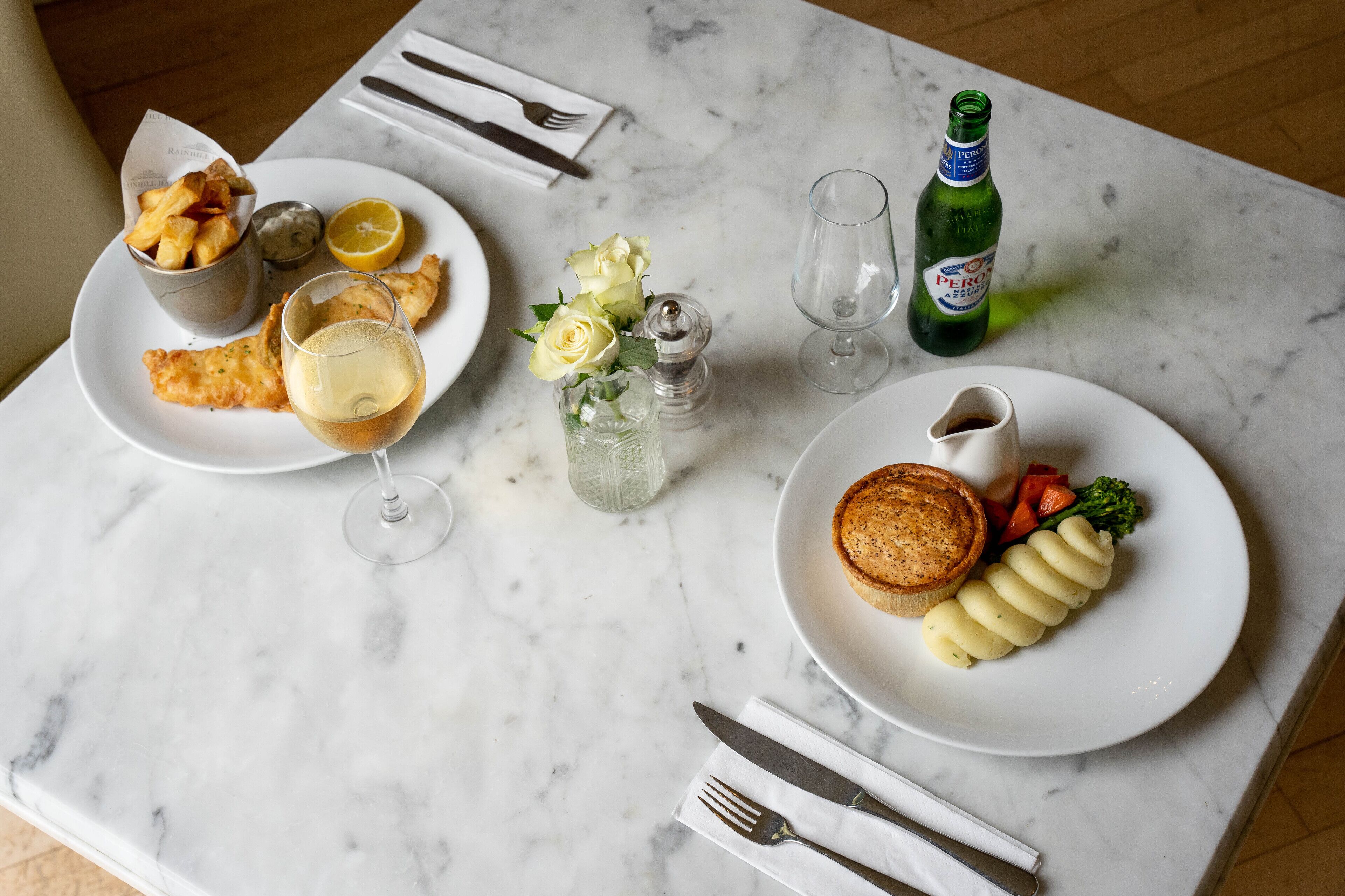 Una mesa de comedor con platos de comida, una botella de cerveza y un salero.