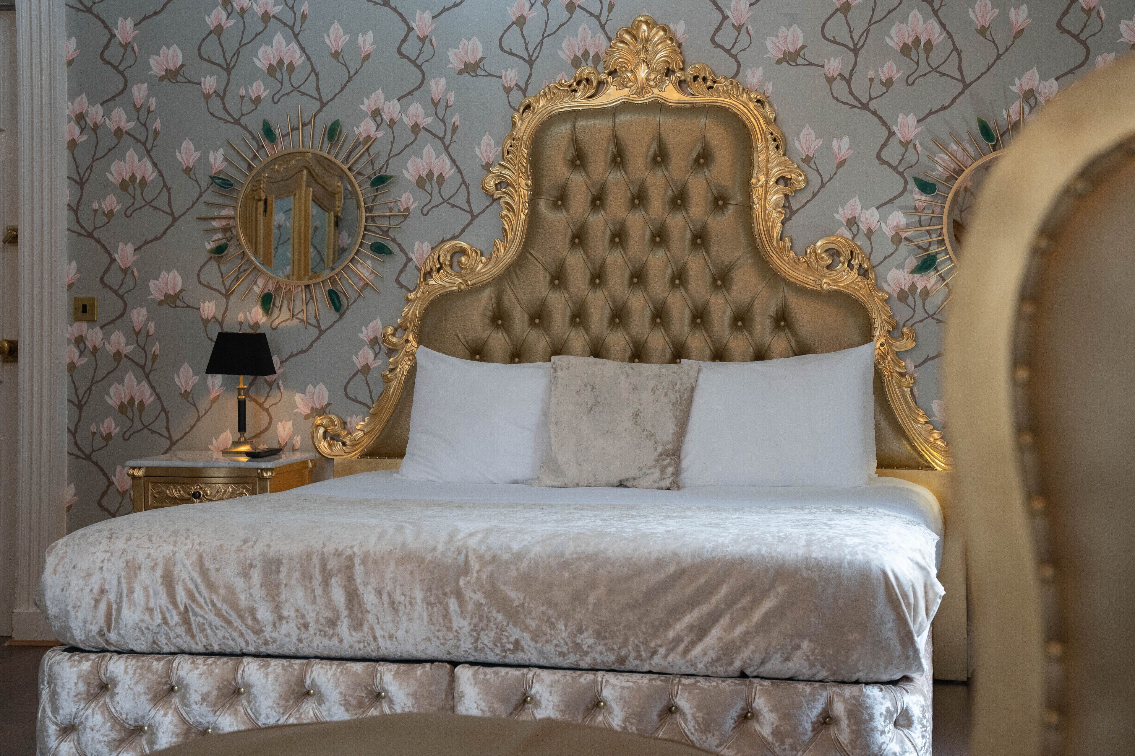 Een luxueuze slaapkamer met een geborduurde hoofdbord, een ronde spiegel en behang met een bloemenpatroon.