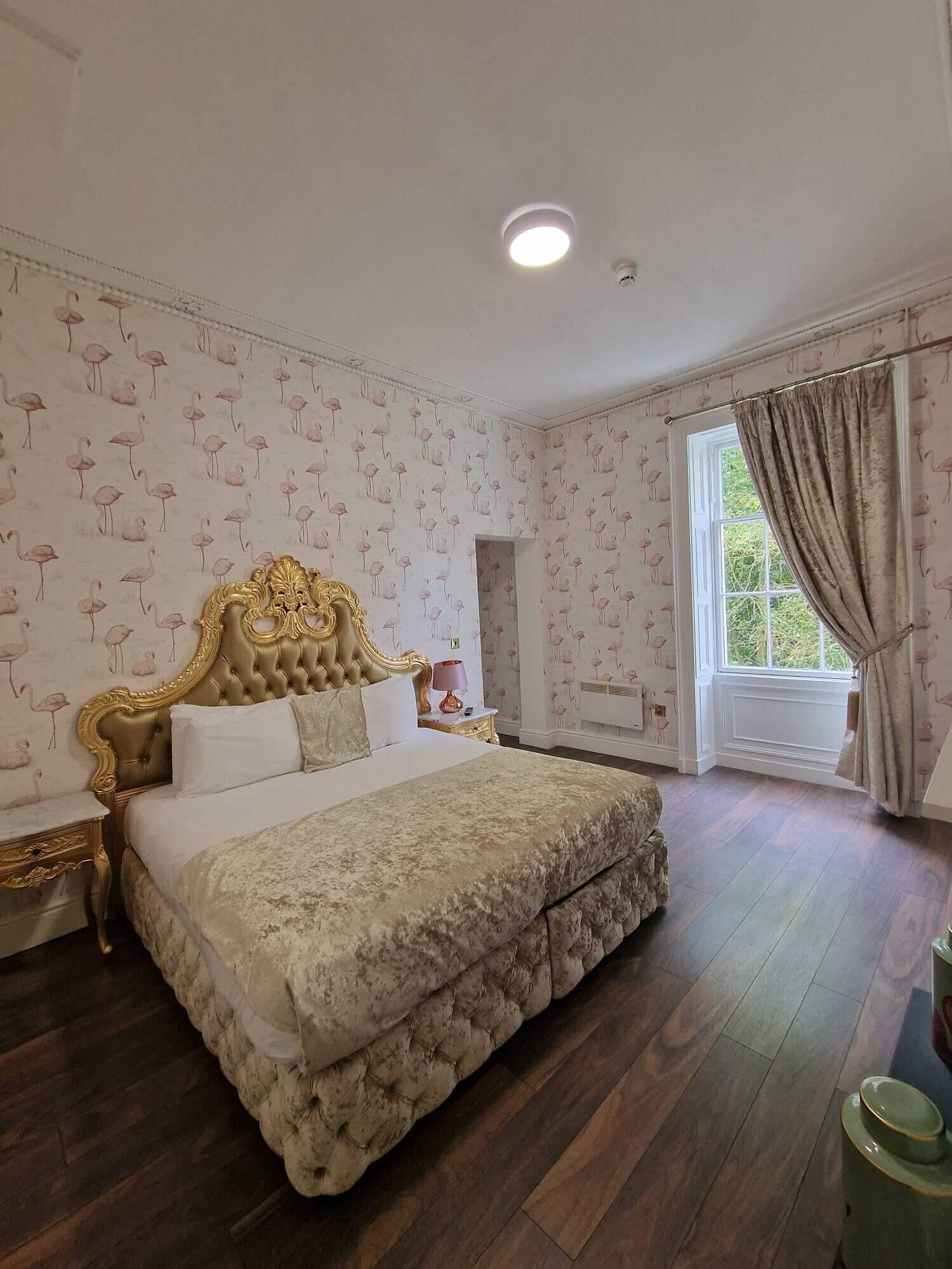 A bedroom with a large bed, a nightstand, a dresser, and a window with curtains.