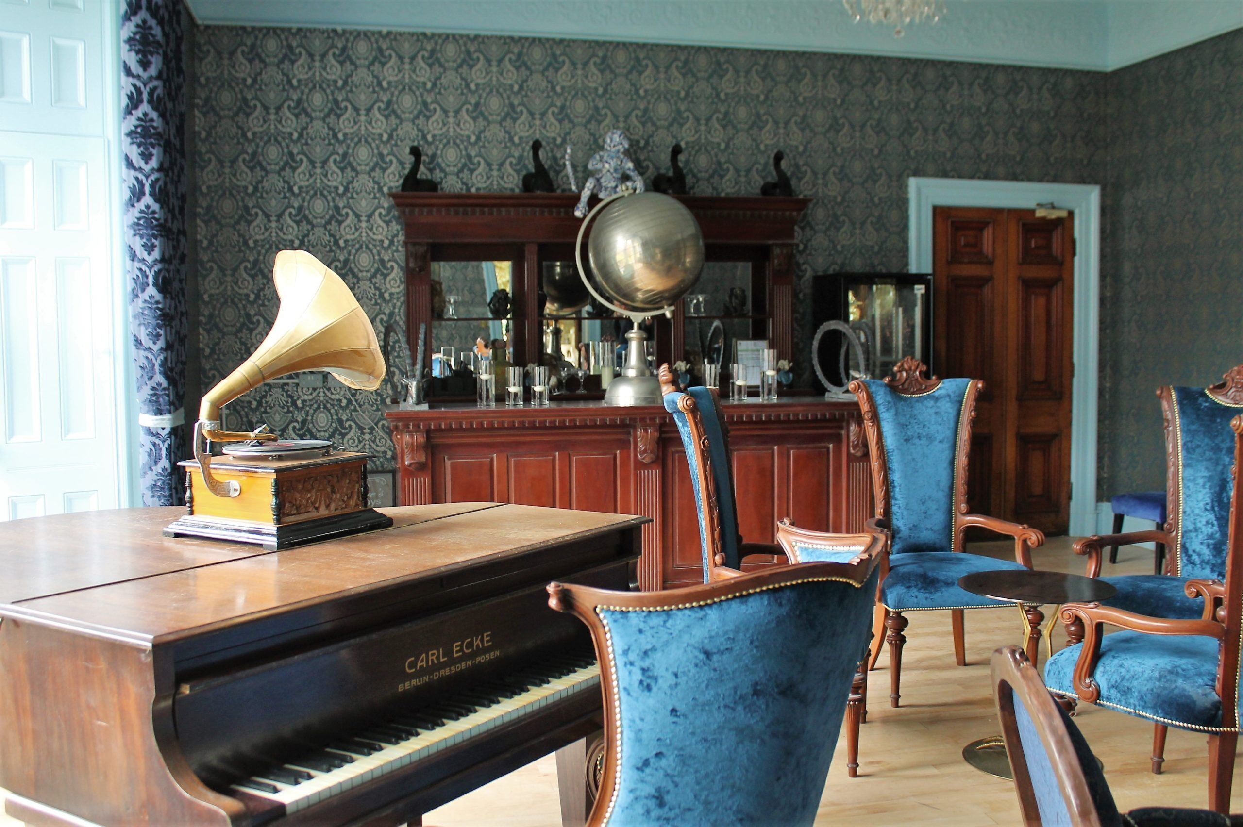 A room with a grand piano, blue velvet chairs, and a decorative lamp.