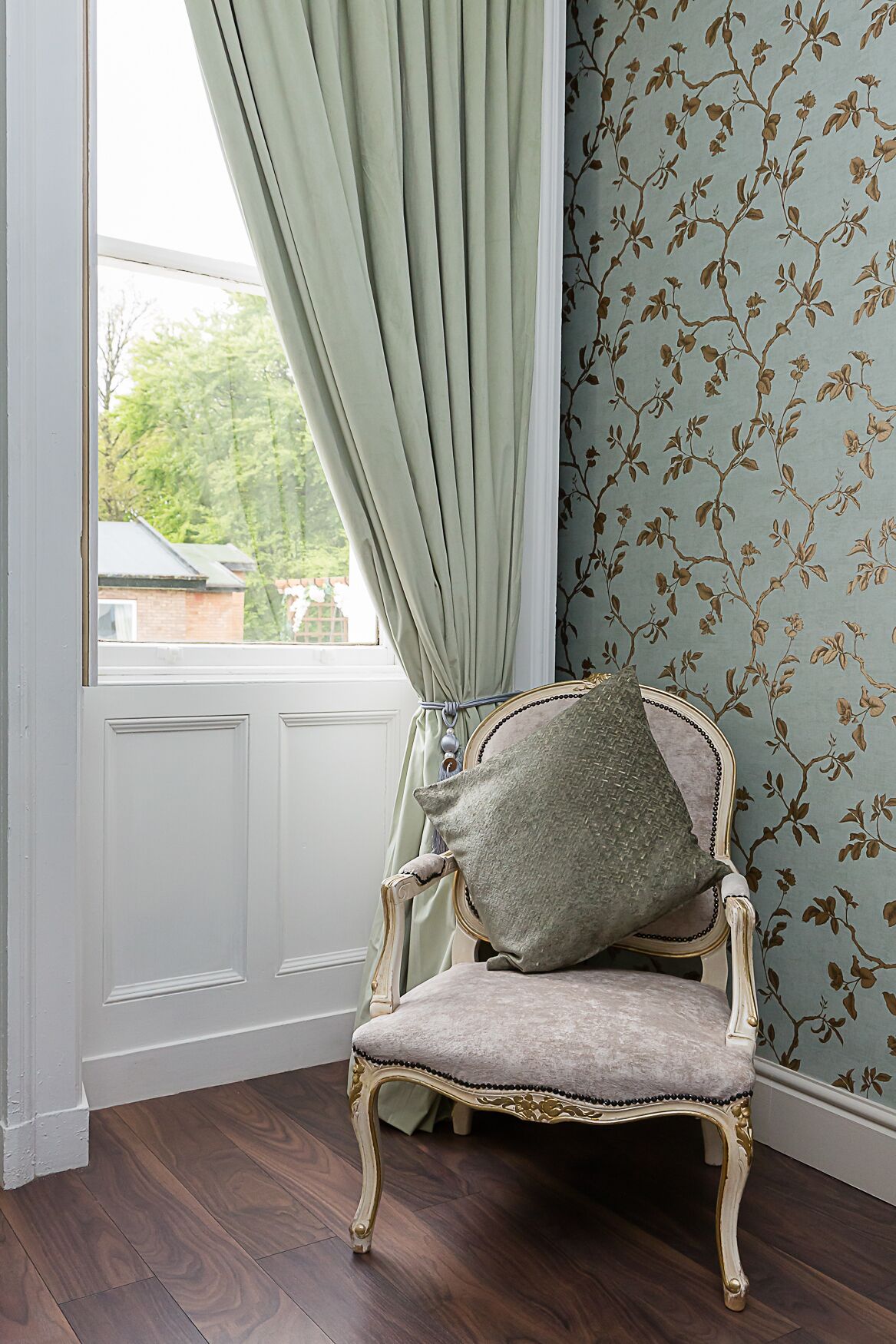 A room with a window, a chair, and a wall with floral wallpaper.