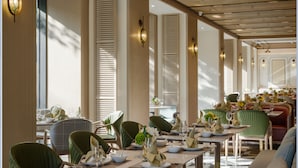 A restaurant with multiple dining tables and chairs, featuring a modern interior with wooden beams and pendant lighting.