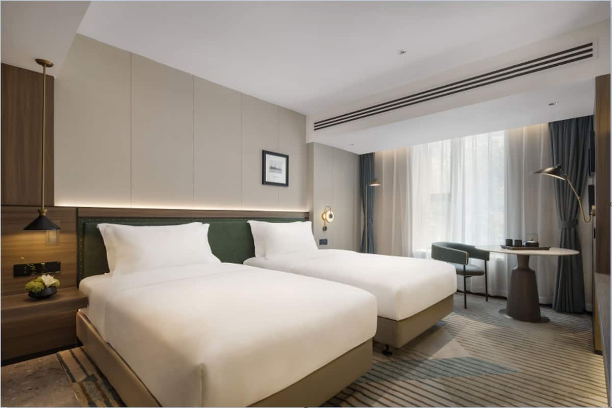 A hotel room with two beds, a desk, a chair, and a large window with curtains.