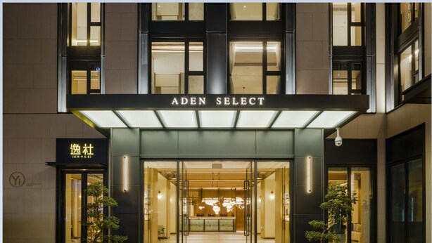 The exterior of the Aden Select hotel with a modern facade, large glass entrance, and potted plants at the entrance.