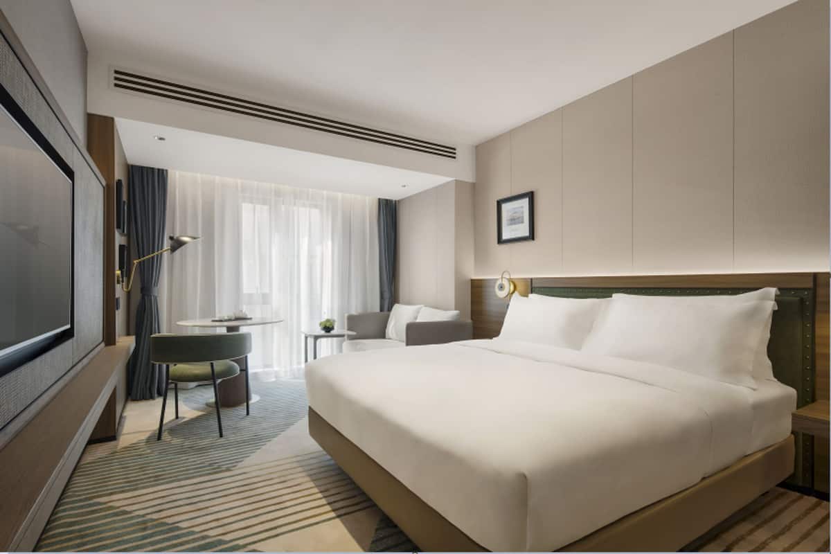 A modern hotel room with a large bed, a television, a desk, and a chair.