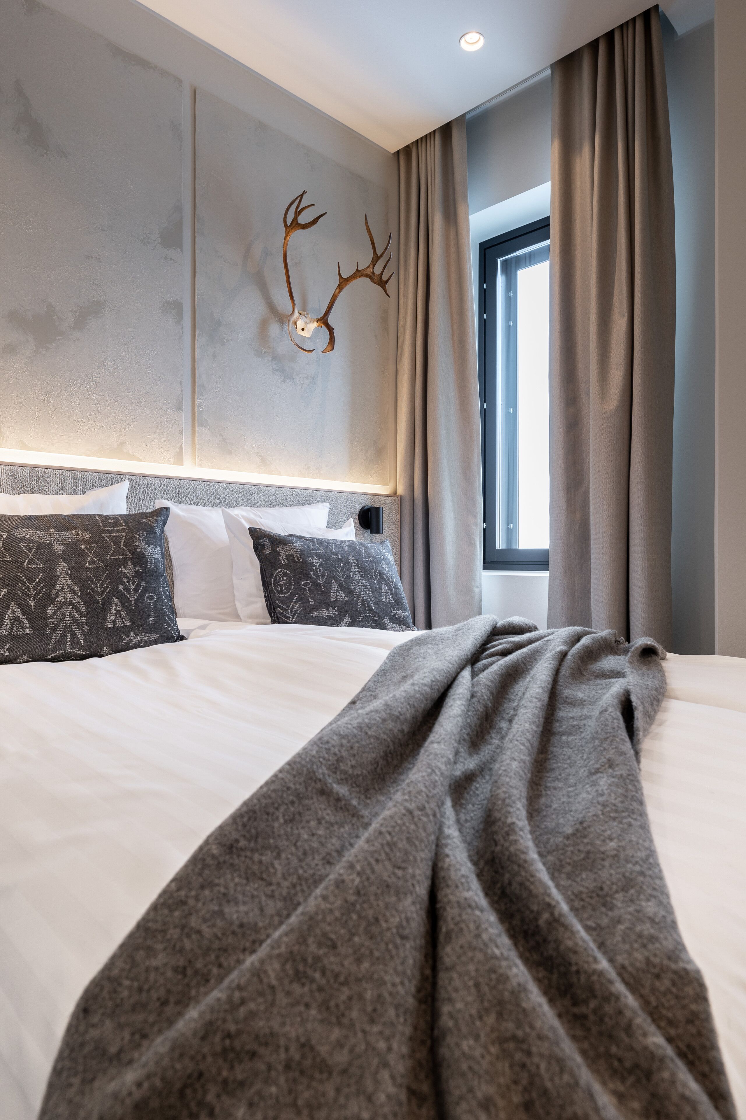 Una camera da letto moderna con un letto grande, una testiera con illuminazione integrata, una decorazione a corna di cervo appesa al muro e una finestra con tende.