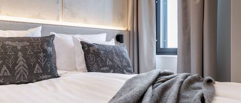 A modern bedroom with a large bed, a headboard with built-in lighting, a wall-mounted deer antler decoration, and a window with curtains.