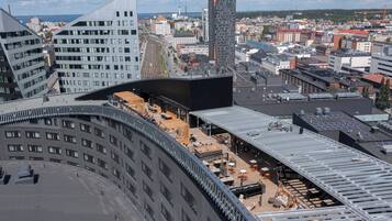 A modern building with a curved facade, a rooftop terrace with outdoor seating, and a view of the cityscape.
