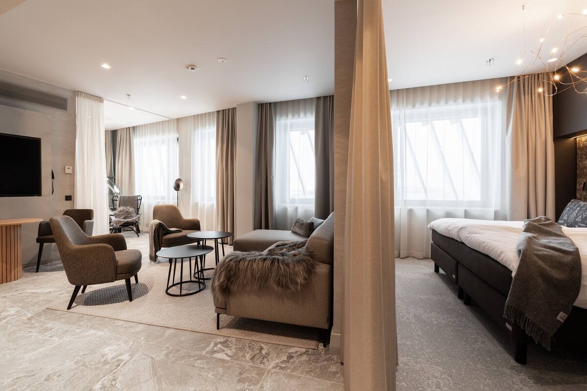 Ein modernes Hotelzimmer mit einem großen Bett, einer Couch, einem Sessel, einem kleinen Tisch und einem Fernseher.