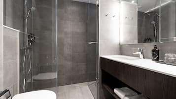 A modern bathroom with a glass-enclosed shower, a white toilet, a dark wood vanity, and a large mirror.