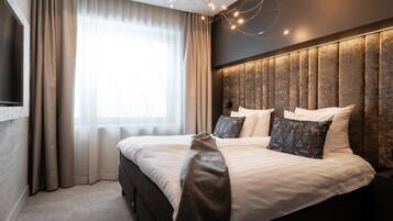 Une chambre à coucher moderne avec un grand lit, une tête de lit ornée de panneaux verticaux et une grande fenêtre avec des rideaux légers.