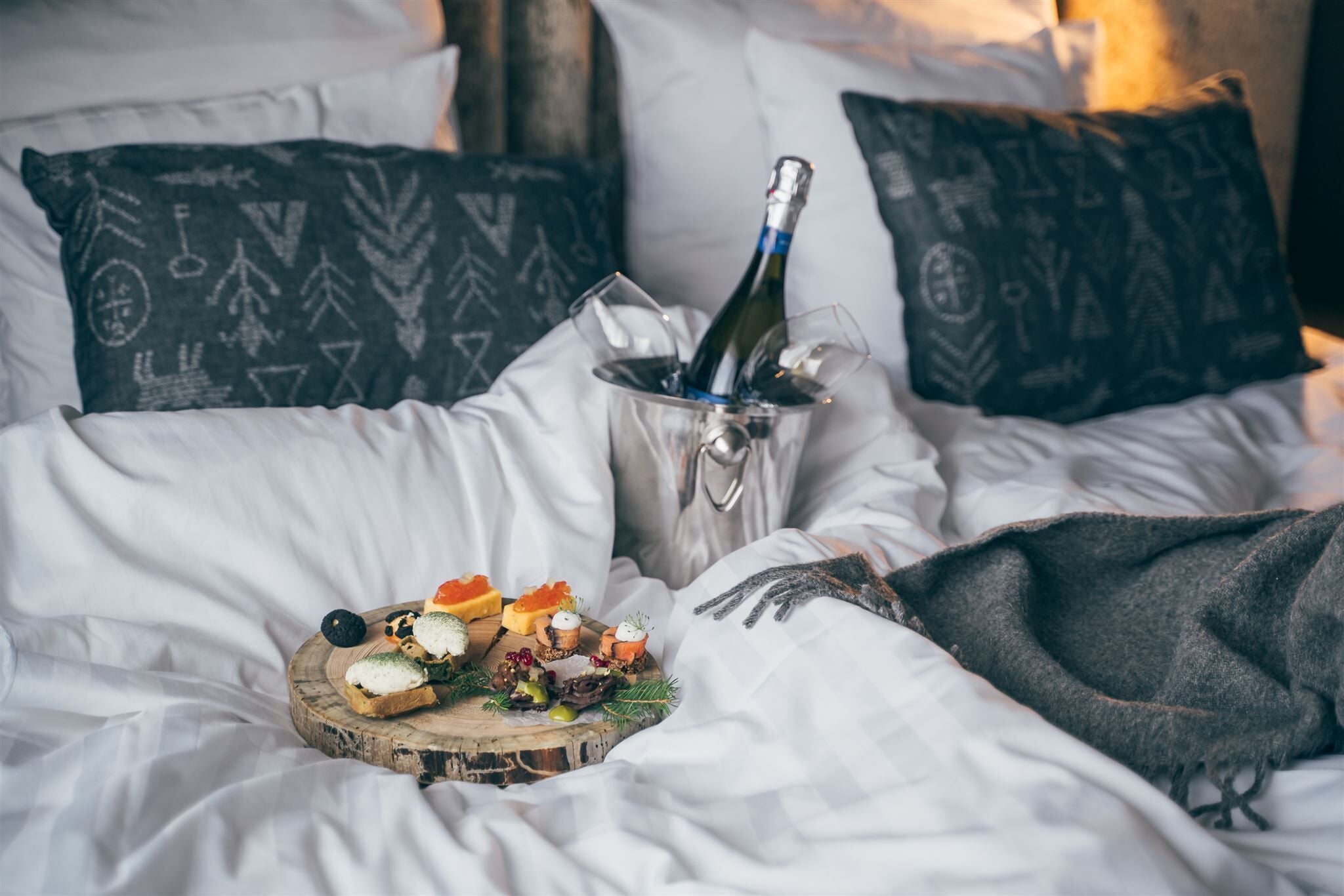 Un lit avec du linge de maison blanc, une bouteille de champagne et un assortiment de fruits.