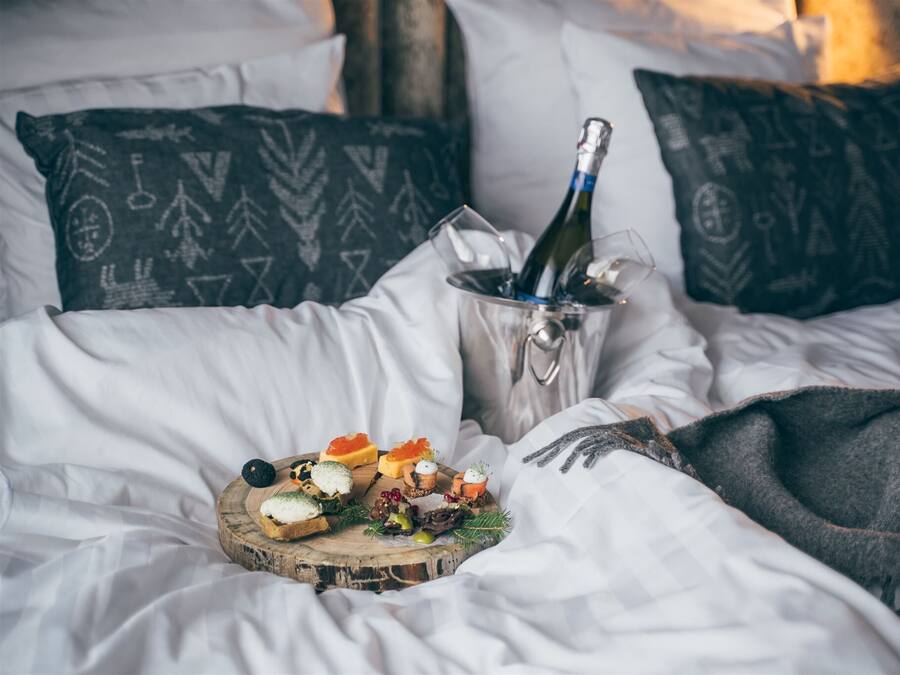 Un lit avec du linge de maison blanc, une bouteille de champagne et un assortiment de fruits.