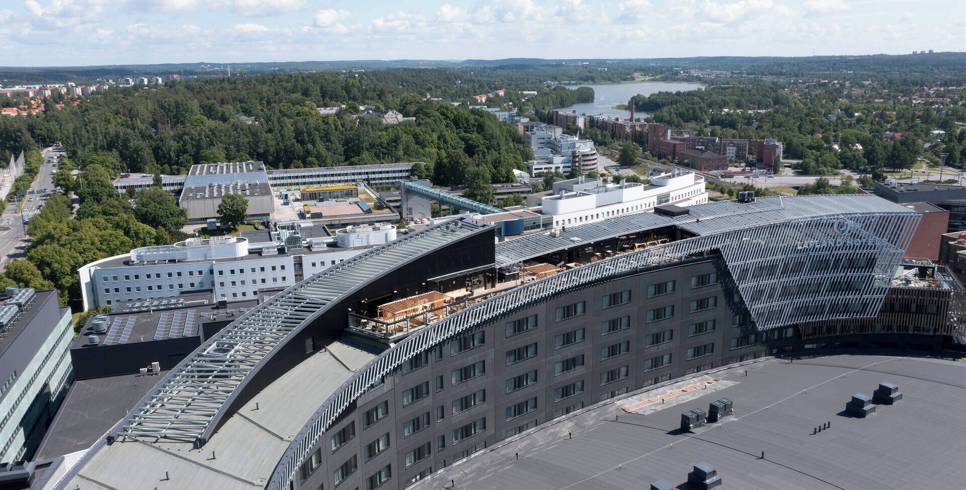 A modern building with a curved roof, multiple floors, and a flat rooftop area.