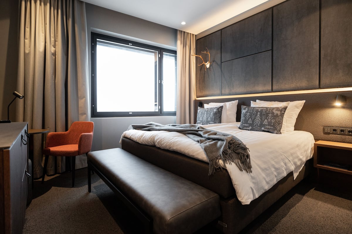 Ein modernes Hotelzimmer mit einem großen Bett, einer Bank, einem Schreibtisch und einem Fenster mit Vorhängen.