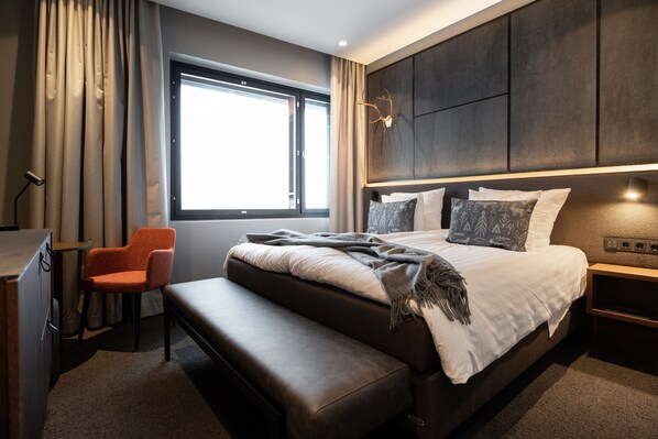 A modern hotel room with a large bed, a bench, a desk, and a window with curtains. - Lapland Hotels Arena (Tampere)