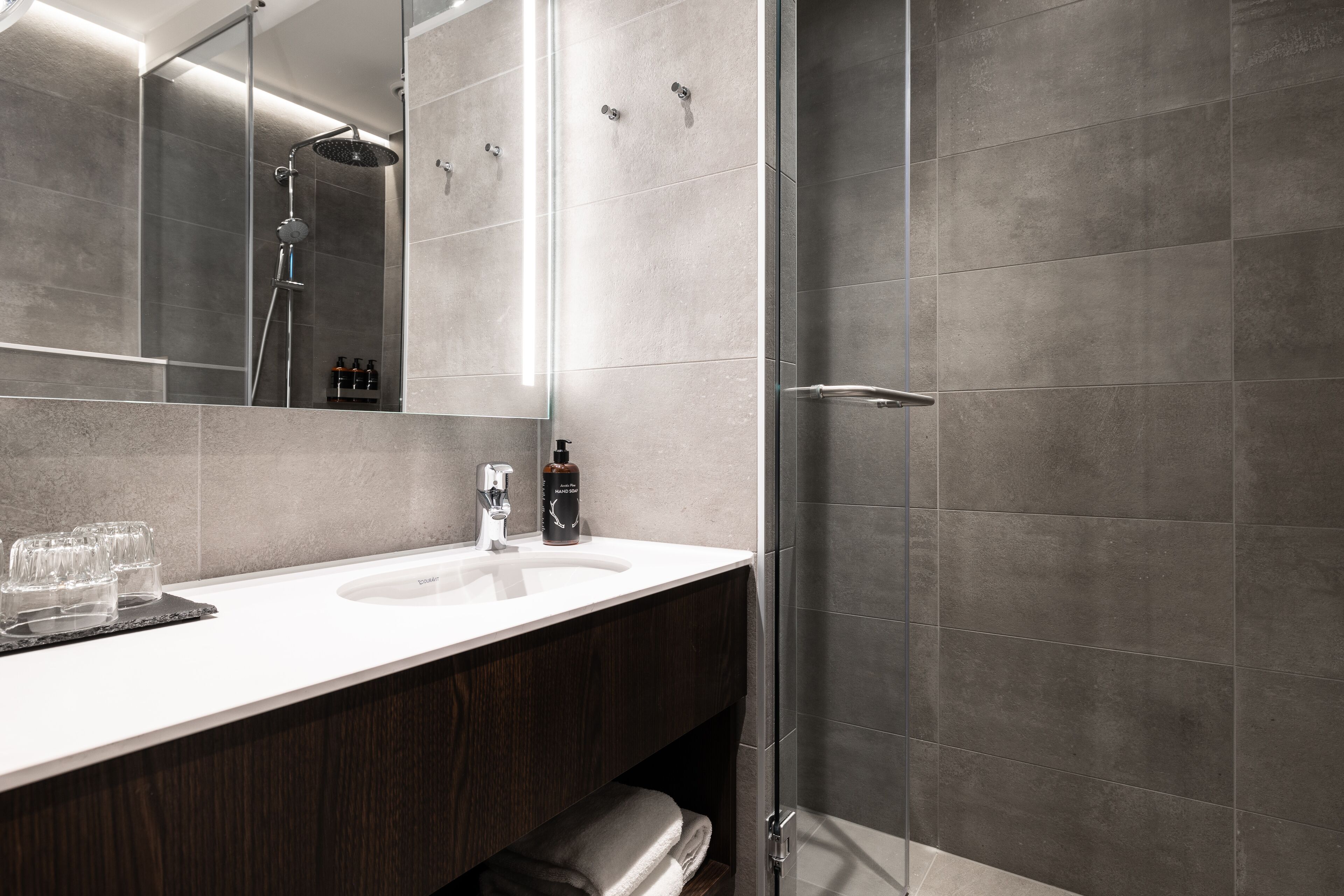 Een moderne badkamer met een grote spiegel, een witte wastafel en een douchegedeelte.