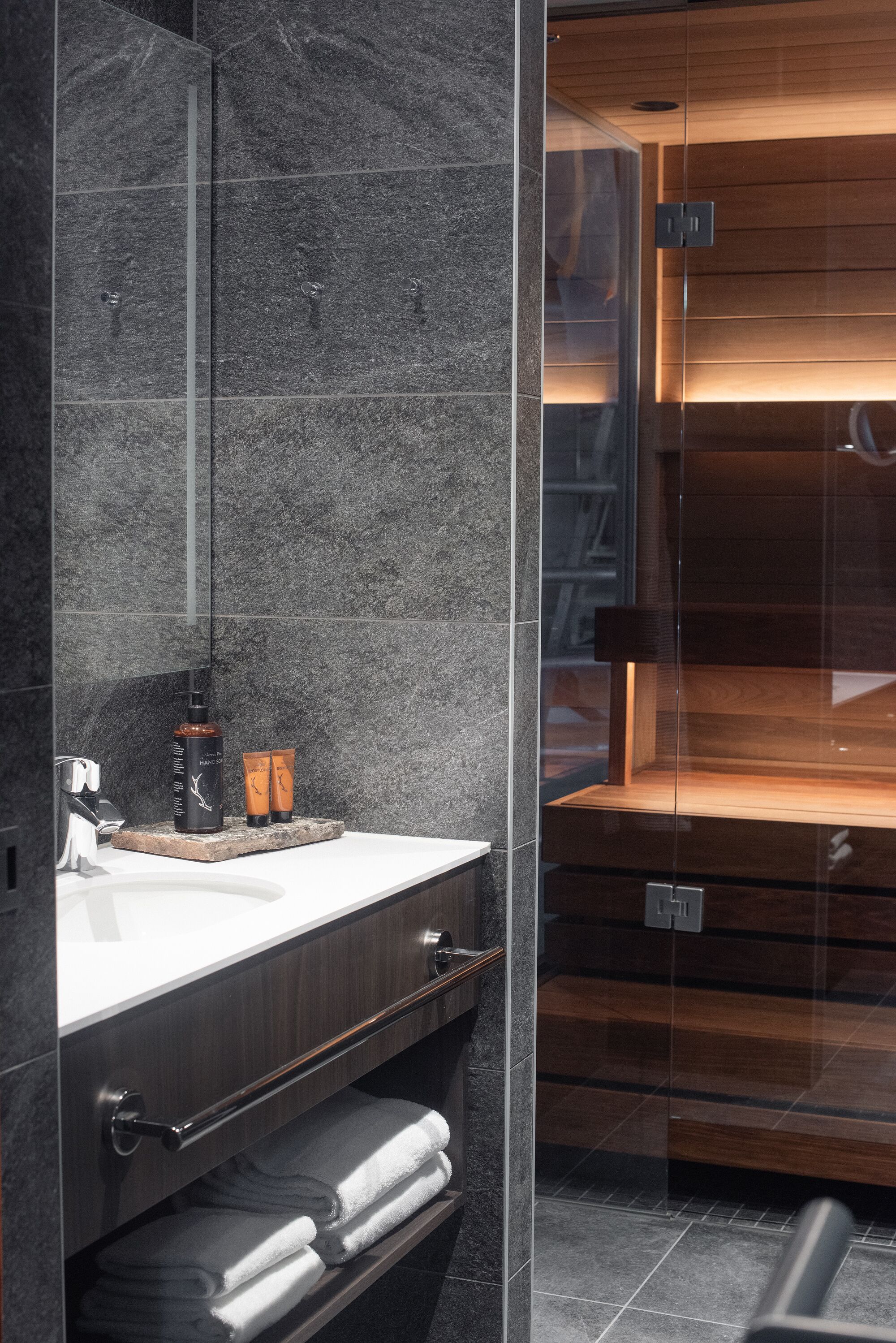 Un baño moderno con pared de mármol, tocador de madera y cabina de ducha de vidrio.