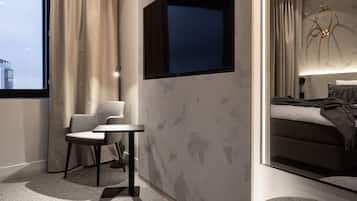 A modern hotel room with a large window, a bed with a headboard, a desk, and two chairs.