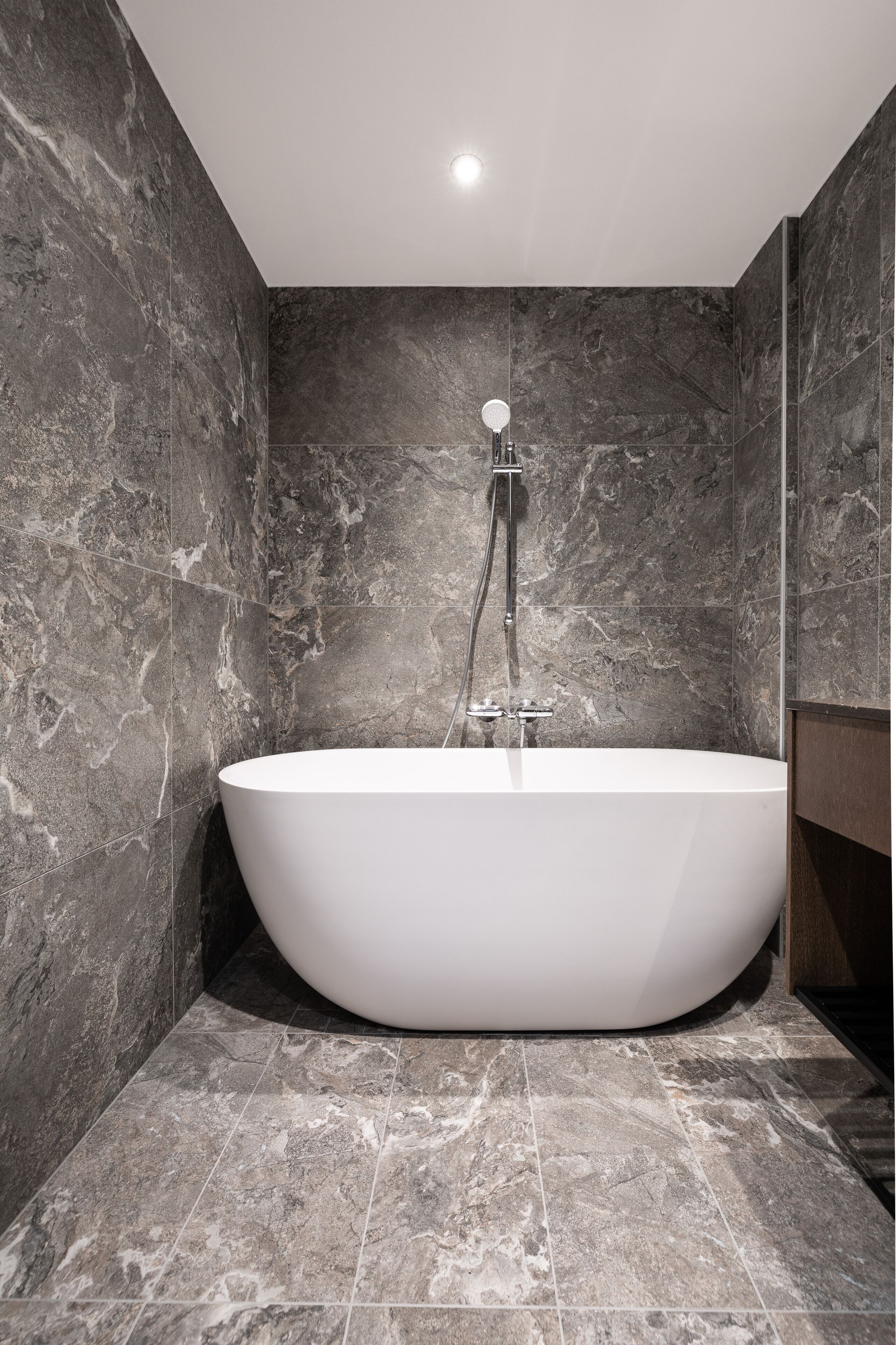 A modern bathroom with a freestanding bathtub, marble walls, and a tiled floor.