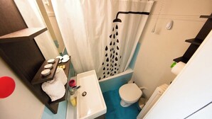 A compact bathroom with a shower curtain, a sink, a toilet, and a shelf with toiletries. - Dimitsanas25-Startupper's Pad in real Athenian nei (Athens)