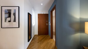 Un couloir moderne avec un plancher en bois, une œuvre d’art encadrée sur le côté gauche et une porte en bois au fond.
