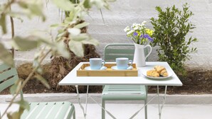 Ein kleiner Tisch im Freien mit einer weißen Karaffe, zwei blauen Tassen, einer Platte mit Croissants und einer weiteren Croissantplatte.