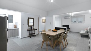 A modern kitchen with a built-in refrigerator, a dining area with a wooden table and chairs, and a living space with a sofa and a TV.