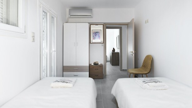 A hotel room with two beds, a wardrobe, a chair, and an air conditioning unit.
