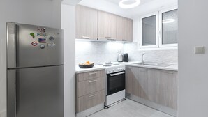 A modern kitchen with a stainless steel refrigerator, wooden cabinets, a built-in oven, and a window above the sink.