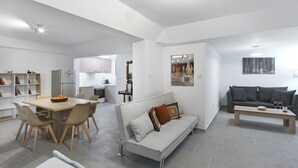 A modern living room with a sofa, a dining table with chairs, a kitchen area, and a small seating area with a bench.